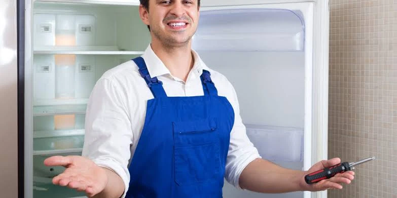 Appliance technician holding a screwdriver beside an open refrigerator
